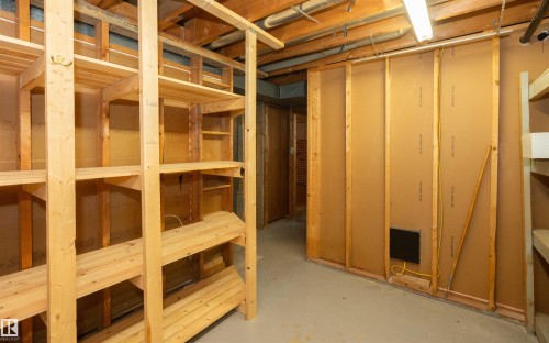 Unfinished basement space featuring exposed wooden beams, concrete flooring, and extensive built-in wooden shelving for storage - 4414 54 Avenue, Barrhead, AB - Indoor