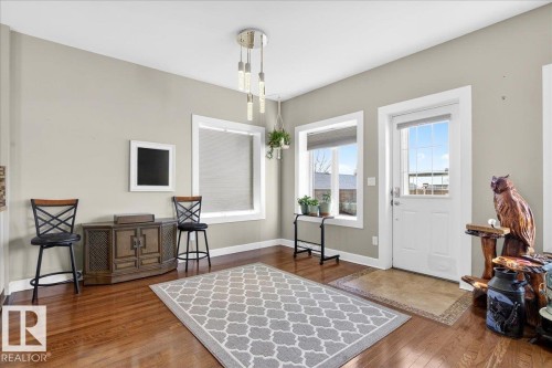 Polished wood-finish flooring throughout, featuring a modern multi-light pendant fixture, white trim, and a white paneled entry door with frosted glass - 5019 48 Avenue, Chipman, AB - Indoor