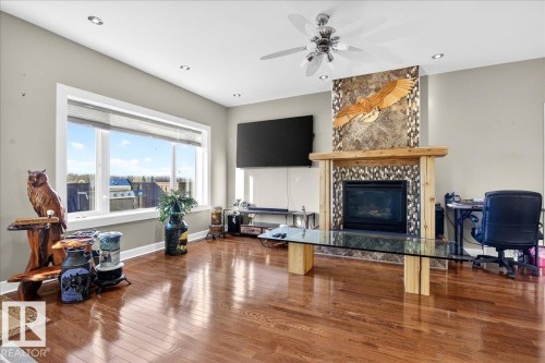 Living area featuring hardwood flooring, a fireplace with a stone surround and wood mantel, a ceiling fan with integrated lighting, recessed lighting, and a large picture window - 5019 48 Avenue, Chipman, AB - Indoor Photo Showing Living Room With Fireplace