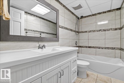 Bathroom featuring a white vanity with integrated sink, a framed rectangular mirror, a bathtub with shower, and tiled walls with decorative mosaic accents - 5019 48 Avenue, Chipman, AB - Indoor Photo Showing Bathroom
