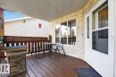 Covered porch featuring wood-finish decking, stone-faced exterior wall accents, a white storm door with decorative glass, white vinyl siding, and a lattice privacy screen - 5019 48 Avenue, Chipman, AB  - Outdoor With Deck Patio Veranda With Exterior 