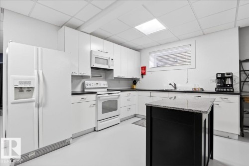Kitchen featuring white cabinetry, dark countertops, white appliance suite, and a freestanding island with a light-colored stone top - 5019 48 Avenue, Chipman, AB - Indoor Photo Showing Kitchen