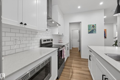 Modern kitchen featuring white shaker cabinetry, light-toned countertops, a white subway tile backsplash, and wood-finish flooring - 22836 94 Avenue, Edmonton, AB 
