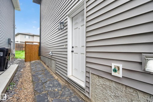 Grey horizontal siding exterior featuring a white paneled door with black hardware, a black wall-mounted lantern light fixture, and a stone slab pathway - 22836 94 Avenue, Edmonton, AB 