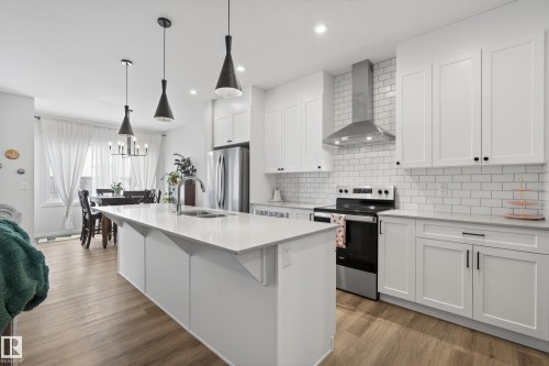 Gourmet kitchen featuring a waterfall island with an undermount sink, white shaker cabinetry, stainless steel appliances, subway tile backsplash, and wood-finish flooring - 22836 94 Avenue, Edmonton, AB 