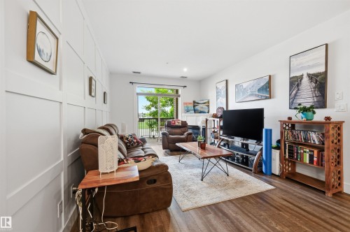 Living area featuring wood-finish flooring, a white paneled accent wall, and a sliding glass door to an outdoor balcony - 217 2503 Hanna Crescent, Edmonton, AB 