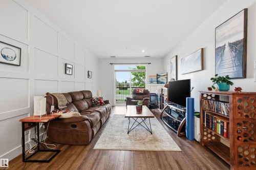 Spacious living area featuring a board and batten accent wall, wood-finish flooring, a glass sliding door, and recessed lighting - 217 2503 Hanna Crescent, Edmonton, AB 