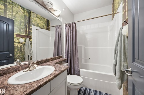 Bathroom featuring a white vanity with a drop-in sink, stone-finish countertop, and wall-mounted mirror - 217 2503 Hanna Crescent, Edmonton, AB 