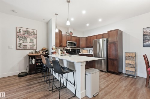 Spacious kitchen featuring an island with white countertop, rich wood-finish cabinetry, stainless steel appliances, and wood-finish flooring - 217 2503 Hanna Crescent, Edmonton, AB 