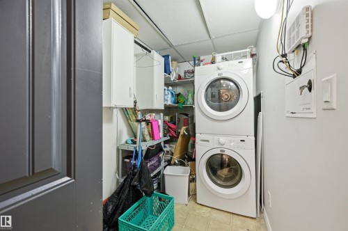 Laundry area featuring stacked front-loading appliances, overhead cabinetry, and built-in shelving - 217 2503 Hanna Crescent, Edmonton, AB 