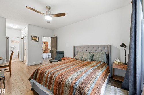 Bedroom featuring wood-finish flooring, a contemporary ceiling fan with integrated lighting, and a tufted upholstered headboard - 217 2503 Hanna Crescent, Edmonton, AB 