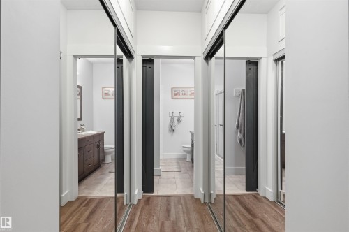 Hallway with wood-finish flooring and three sets of mirrored sliding closet doors - 217 2503 Hanna Crescent, Edmonton, AB 