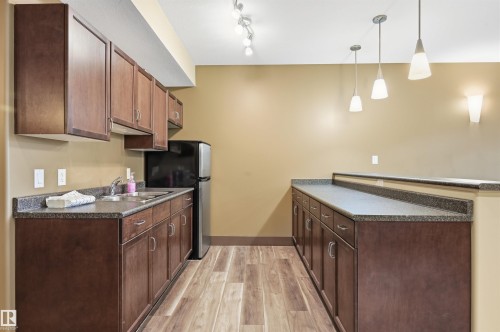 Kitchenette featuring wood-finish flooring, dark wood cabinetry, and speckled countertops - 217 2503 Hanna Crescent, Edmonton, AB 