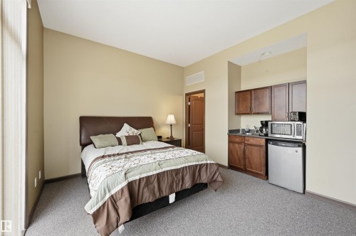 Studio living space featuring a built-in kitchenette with wood-finish cabinetry and a compact refrigerator - 217 2503 Hanna Crescent, Edmonton, AB 