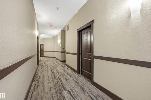Hallway featuring wood-finish flooring, two-tone paint, dark trim, and sconce lighting - 217 2503 Hanna Crescent, Edmonton, AB 