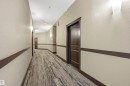 Hallway featuring wood-finish flooring, two-tone paint, dark trim, and sconce lighting - 217 2503 Hanna Crescent, Edmonton, AB 