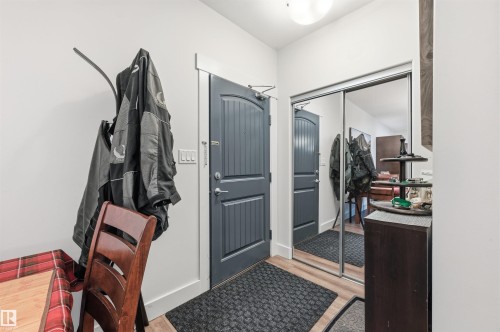 Entryway featuring a dark gray paneled door with white trim, wood-finish flooring, a full-height mirrored closet, and a flush-mount ceiling light - 217 2503 Hanna Crescent, Edmonton, AB 