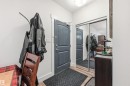 Entryway featuring a dark gray paneled door with white trim, wood-finish flooring, a full-height mirrored closet, and a flush-mount ceiling light - 217 2503 Hanna Crescent, Edmonton, AB 