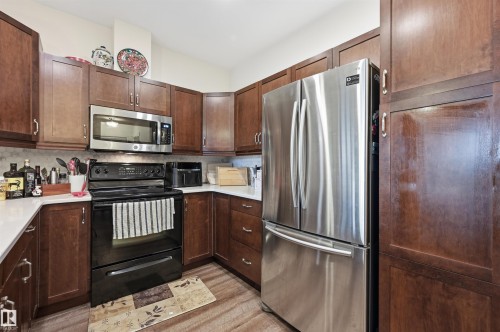 Kitchen featuring wood-finish cabinetry, stainless steel refrigerator, black electric range, and solid surface countertops - 217 2503 Hanna Crescent, Edmonton, AB 