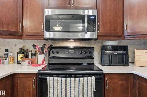 Kitchen featuring wood cabinetry, stainless steel microwave, black electric range, white countertops, and a hexagon tile backsplash - 217 2503 Hanna Crescent, Edmonton, AB 