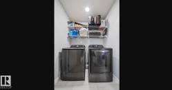 Laundry area featuring a ceiling-mounted light fixture, light gray walls, light tile flooring, and integrated wire shelving - 