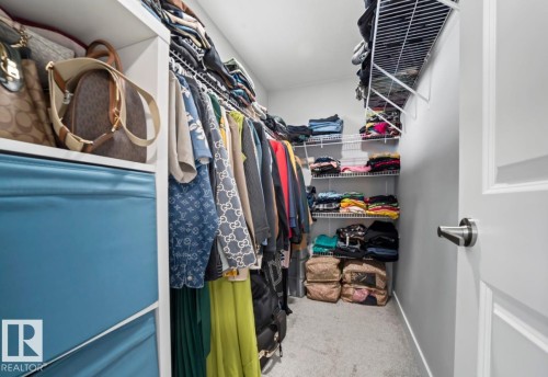 Walk-in closet featuring built-in white wire shelving, carpeting, and a panel door with brushed nickel hardware - 2153 Maple Road, Edmonton, AB 