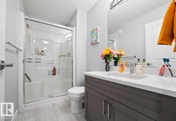 Contemporary bathroom featuring a spacious shower enclosure with sliding glass doors, a vanity with a white countertop and undermount sink, a large wall-mounted mirror, a two-door vanity cabinet with brushed nickel hardware, and light-toned tile flooring - 