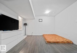 Spacious room featuring wood-finish flooring, white walls, and an overhead lighting fixture - 