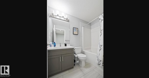 Modern bathroom featuring a single vanity with a white countertop and gray cabinetry, a white toilet, and a white bathtub with subway tile surround - 2153 Maple Road, Edmonton, AB 