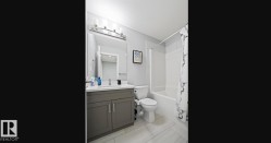 Modern bathroom featuring a single vanity with a white countertop and gray cabinetry, a white toilet, and a white bathtub with subway tile surround - 
