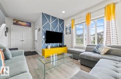 Spacious living area featuring wood-finish flooring, a geometric accent wall, and ample natural light from large windows - 