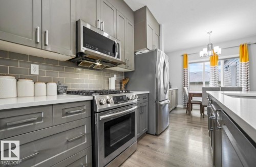 Contemporary kitchen featuring gray cabinetry, stainless steel appliances, white countertops, and a gray subway tile backsplash - 2153 Maple Road, Edmonton, AB 