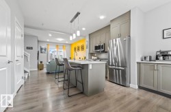 Open-concept kitchen featuring an island with seating, stainless steel appliances, grey cabinetry, and wood-finish flooring - 