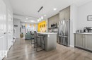 Open-concept kitchen featuring an island with seating, stainless steel appliances, grey cabinetry, and wood-finish flooring - 2153 Maple Road, Edmonton, AB 