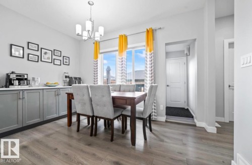 Dining area featuring wood-finish flooring, a contemporary chandelier, and a large window - 2153 Maple Road, Edmonton, AB 