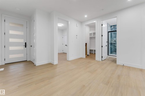 Contemporary interior featuring wood-finish flooring, recessed lighting, and a modern entryway door with horizontal frosted glass inserts - 131 24 Street, Edmonton, AB 