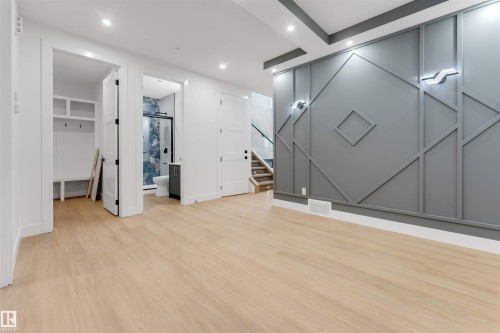 Spacious interior featuring wide-plank wood-finish flooring and a distinctive accent wall with geometric molding - 131 24 Street, Edmonton, AB 