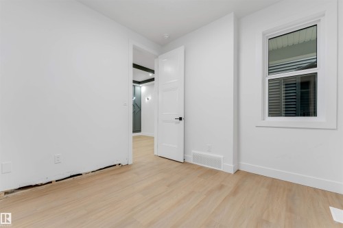 Room featuring light wood-finish flooring, white walls, a white door with black hardware, and a window with horizontal blinds - 131 24 Street, Edmonton, AB 