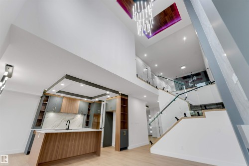 Open-concept living space with a contemporary kitchen, two-story ceiling, and a prominent floating staircase with glass railings - 131 24 Street, Edmonton, AB 