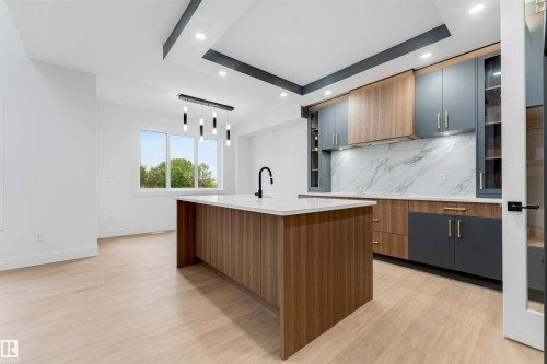 Modern kitchen featuring a large central island with a white countertop and dark-finish faucet - 131 24 Street, Edmonton, AB 