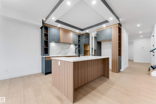 Open-concept kitchen featuring an island with a light wood-finish base and light countertop, dual-toned cabinetry, a modern black faucet, and recessed lighting - 131 24 Street, Edmonton, AB 