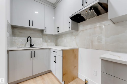 Modern kitchen featuring light gray cabinetry with black hardware, white countertops, a black gooseneck faucet, an under-mount sink, and a tile backsplash - 131 24 Street, Edmonton, AB 