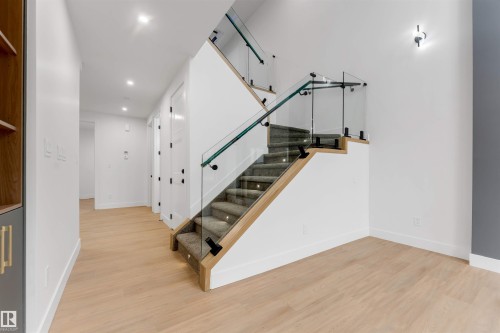 Hardwood-finish flooring extending to a carpeted staircase with glass railings and wood handrails - 131 24 Street, Edmonton, AB 
