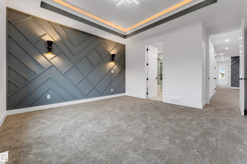 Spacious room featuring a geometric accent wall with integrated sconce lighting, plush gray carpeting, and a tray ceiling with cove lighting - 131 24 Street, Edmonton, AB 