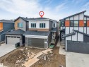 Modern two-story residence featuring a gray exterior with contrasting white siding, a dark shingled roof, a dark garage door with horizontal glass panels, and a prominent front entrance with a contemporary door and dark railings - 131 24 Street, Edmonton, AB 