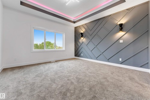 Accent wall with geometric trim and integrated sconces, tray ceiling with recessed lighting, large window with white trim, and gray carpet flooring - 131 24 Street, Edmonton, AB 