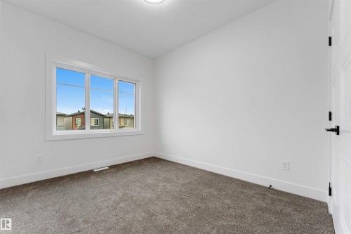 Spacious room featuring a three-pane window, neutral-toned carpeting, white walls, white baseboards, and a white paneled door with black hardware - 131 24 Street, Edmonton, AB 