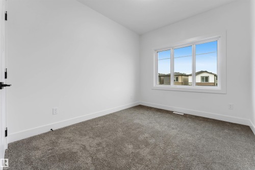 Bright room featuring a large three-panel window, plush gray carpet, white baseboards, and a white door with matte black hardware - 131 24 Street, Edmonton, AB 