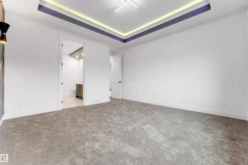 Spacious room featuring neutral carpeting, a recessed ceiling with accent lighting, and crisp white walls - 131 24 Street, Edmonton, AB 