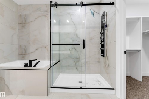 Contemporary bathroom featuring a freestanding tub with matte black fixtures, a glass-enclosed shower with a multi-function shower panel, large format tile walls, and a built-in closet with shelving - 131 24 Street, Edmonton, AB 